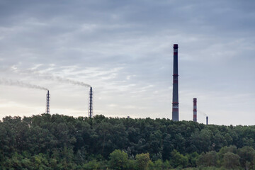 A landscape with a plant from which pipes stick out and release black harmful smoke into the atmosphere, polluting the environment and causing a greenhouse effect.