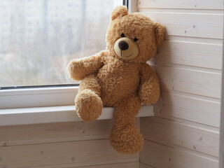 teddy bear children's toy sits on  windowsill overlooking the street