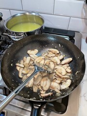 New York. 2021. Chinese meal being cooked using a wok, Chicken stock in a saucepan and mushrooms in a wok to form part of a Chinese meal.