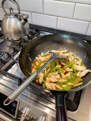 New York. 2021. Chinese meal being cooked using a wok. Cooking using a wok over gas stove, a Chinese meal of chicken and scallions.