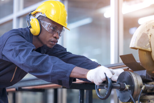 Black male african american workers wear sound proof headphones and yellow helmet working an iron cutting machine in background factory Industrial.