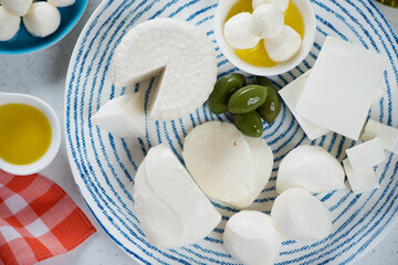 Top view of mozzarella, ricotta and feta cheese with green olives and olive oil on a blue and white...