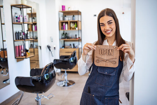 Open For Business. Smiling Worker Holding Open Sign In Her Salon. Happy Young Barber Hanging An Open Sign On Door. Female Owner Is Holding OPEN Sign. She Is Working In Hair Salon