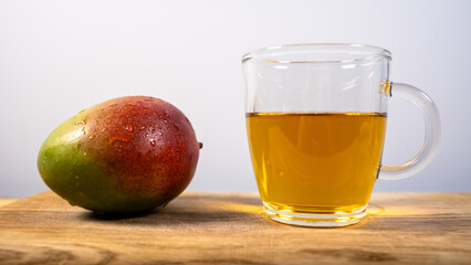 whole mango on a wooden plank with a clear glass cup of tea