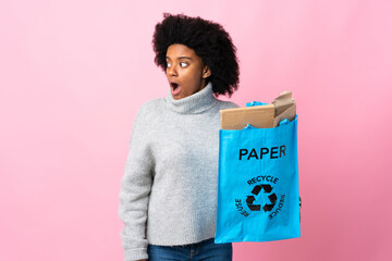 Young African American woman holding a recycle bag isolated on colorful background doing surprise gesture while looking to the side