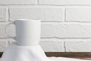 Household utensils, a white cup stands on a napkin against the background of a kitchen stone brick wall of a milky shade, the concept of clean dishes