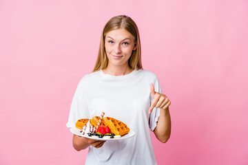 Young russian woman eating a waffle isolated points down with fingers, positive feeling.