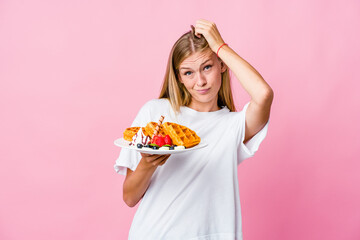 Young russian woman eating a waffle isolated being shocked, she has remembered important meeting.