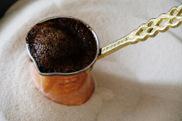 Brewing coffee in copper cezve on sand. Traditional turkish method