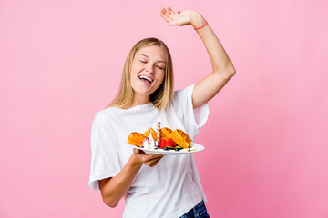 Young russian woman eating a waffle isolated celebrating a special day, jumps and raise arms with energy.