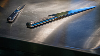 A steel knife and steel fork for cutting sausages lying on a stainless steel countertop.