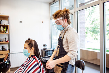 Young woman have hair cutting at hair stylist during pandemic isolation, they both wear protective...