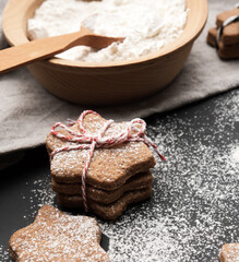 baked star-shaped gingerbread cookie sprinkled with powdered sugar on a black table and ingredients