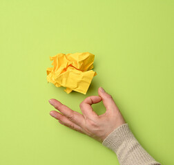 yellow crumpled ball of paper and female hand on a green background