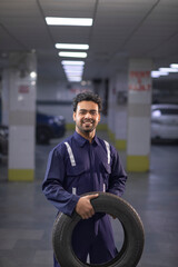 Portrait of smiling mechanic holding a  tyre in auto repair shop	