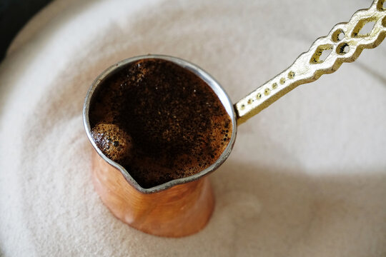 Brewing coffee in copper cezve on sand. Traditional turkish method