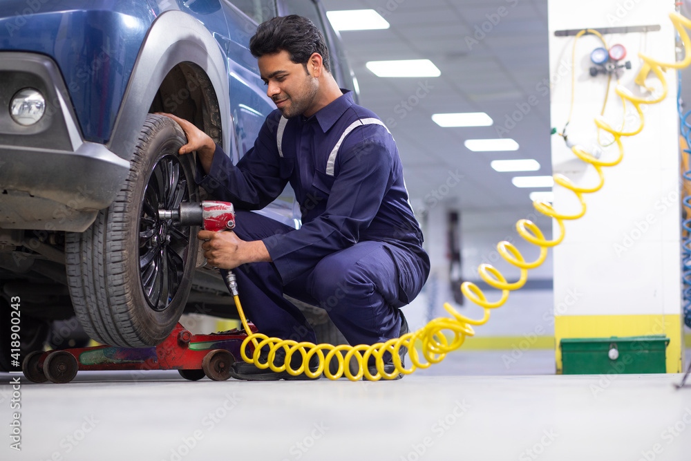 Wall mural A CAR TECHNICIAN USING A BOLTING MACHINE TO LOCK THE BOLTS OF A TYRE AT A WORKSHOP	