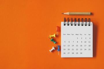 white calendar , thumbtacks and pencil on vivid grunge orange paper background , business or...
