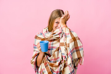 Young russian woman wrapped in a blanket drinking coffee forgetting something, slapping forehead with palm and closing eyes.