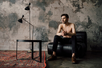 Thoughtful man with scars at the chest resting on armchair at home and pondering about future