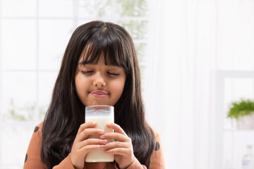 A YOUNG GIRL HOLDING GLASS OF MILK AND DRINKING	