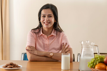 PORTRAIT OF AN ADULT WOMAN SITTING IN FRONT OF A TABLE WITH MILK AND COOKIES ON IT	