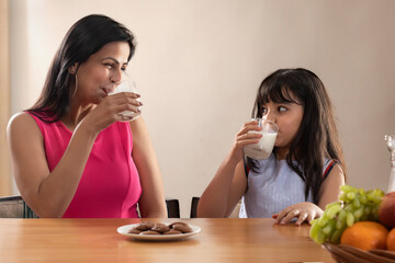 A MODERN MOTHER AND DAUGHTER HAPPILY DRINKING MILK TOGETHER	