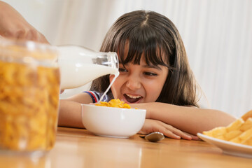 A YOUNG GIRL ENTHUSIASTICALLY LOOKING AT MILK POURED ONTO A BOWL OF CORNFLAKES	