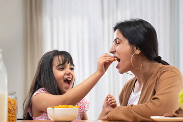 A YOUNG GIRL HAPPILY GIVING NAMKEEN TO MOTHER	