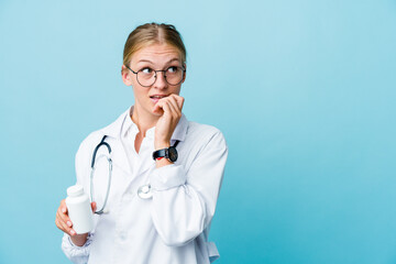 Fototapeta premium Young russian doctor woman holding pills bottle on blue relaxed thinking about something looking at a copy space.