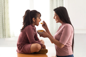 A HAPPY MOTHER GIVING CORNFLAKES TO DAUGHTER	