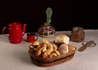 Breads or buns in basket decorated with jam or jelly, coffee and a cactus plant vase