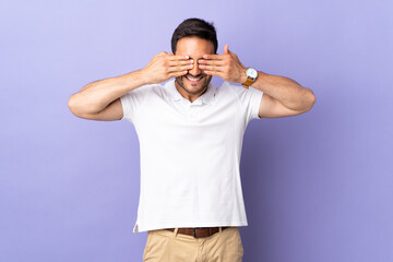 Young handsome man isolated on purple background covering eyes by hands and smiling