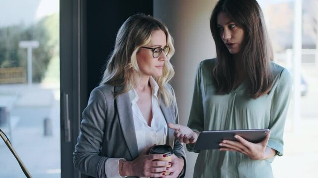 Two businesswomen discussing in office, using digital tablet