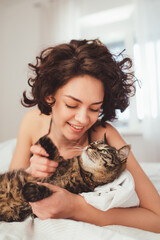 Portrait view of the curly woman relaxing on bed with her striped cat