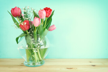 spring bouquet of red and pink tulips flowers in the glass vase over wooden table