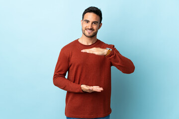 Young handsome man over isolated background holding copyspace imaginary on the palm to insert an ad