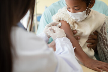 Asian doctor user syringe needle for injection vaccinate,  African American children are being covid vaccinated for prevention coronavirus and flu. Concept of immunization from inoculation