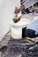 Detail of paint brush and bucket of white paint held by handyman