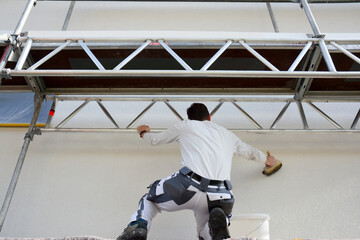 Painter on scaffold prime coating a white facade for renovation