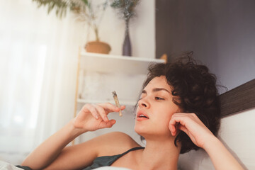 Cropped view of the cute young curly woman smoking  cannabis at the modern bedroom. Bad habits...