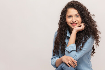 PORTRAIT OF A CURLY HAIRED TEENAGE GIRL LOOKING AT CAMERA AND SMILING	