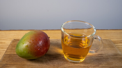 a whole mango with a transparent cup of tea on an eco wooden board. Vegetarian breakfast - top view