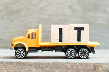 Toy truck hold alphabet letter block in word IT (Abbreviation of information technology) on wood background