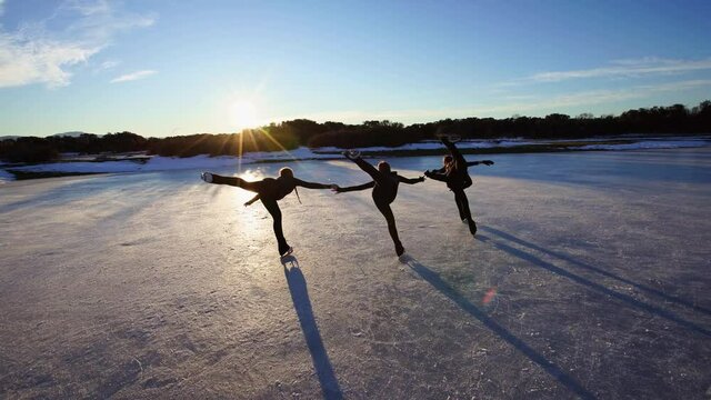 Four young women figure skating on frozen lake at sunset