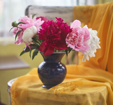 Still life with white and pink peonies in a blue vase on vintaje chair
