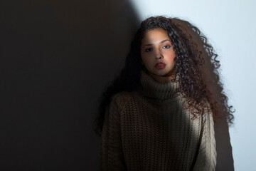 PORTRAIT OF A CURLY HAIRED TEENAGER LOOKING AT CAMERA WITH LIGHT FALLING PARTIALLY ON HER FACE	