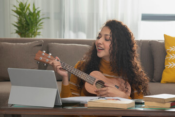 A TEENAGE GIRL SITTING AND PLAYING UKULELE AT HOME	