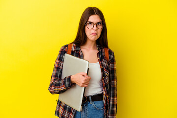 Fototapeta premium Young caucasian student woman holding a laptop isolated on pink background shrugs shoulders and open eyes confused.