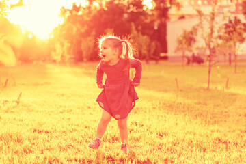 cheerful little girl having fun and jumping at sunset in the evening, flare, sun rays. summer children's games and fun outdoors.